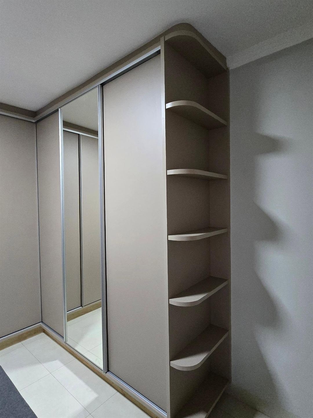 Guarda-roupa planejado com portas de correr, uma delas com espelho, e prateleiras curvas na lateral
